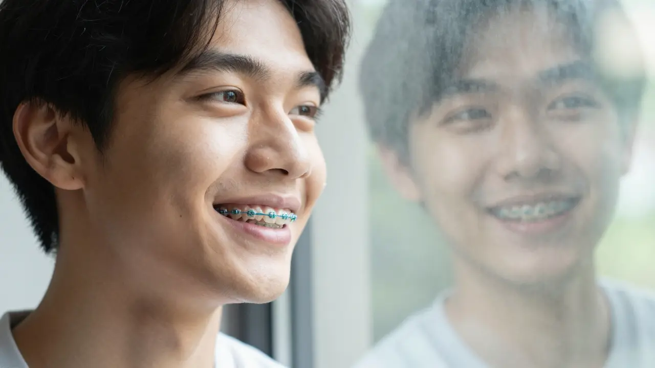 Mladý muž se usmívá s rovnátky a viditelnými gumičkami.